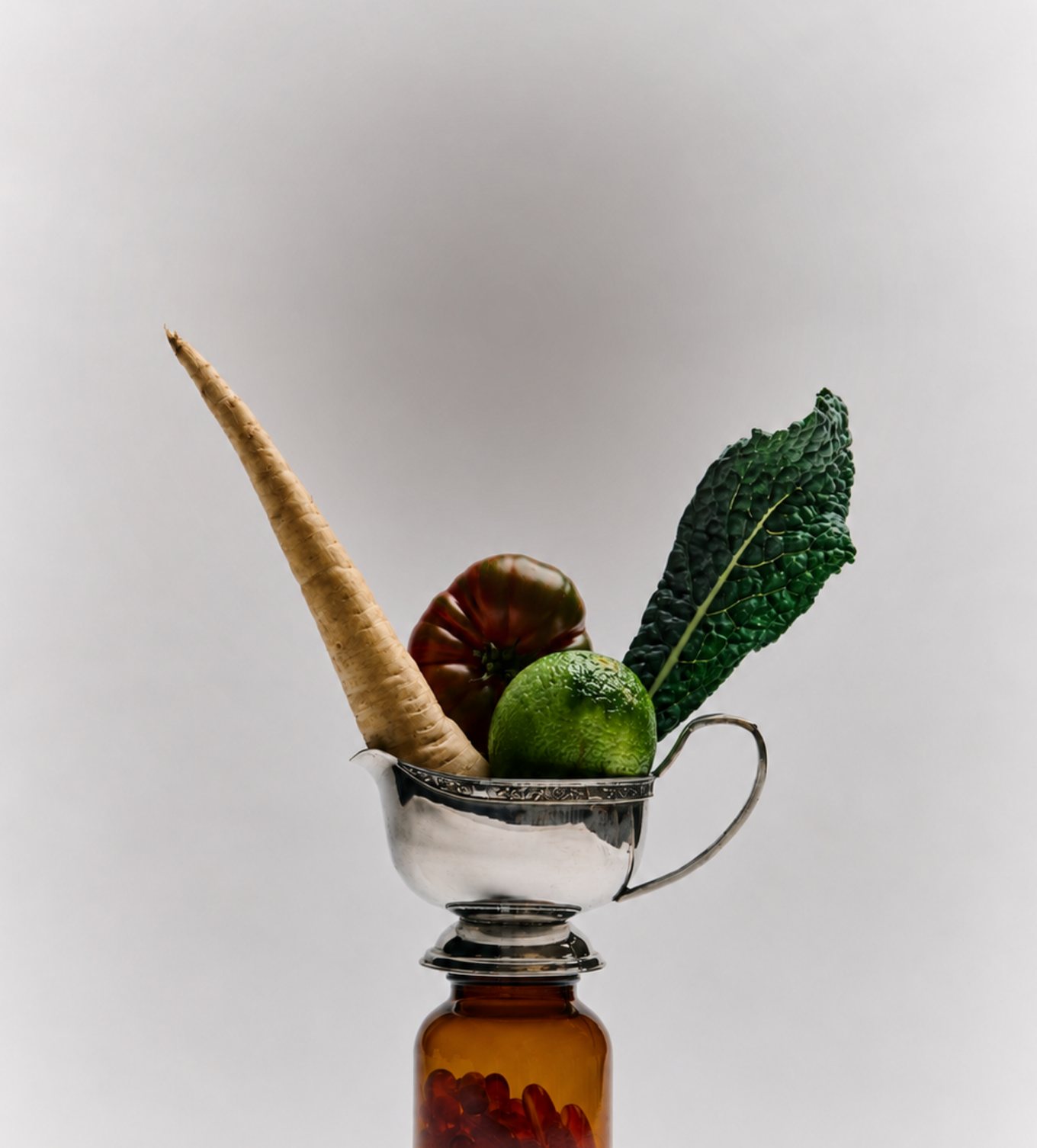 Parsnip, heirloom tomato, lime and cavolo nero in a silver jug atop an amber apothecary bottle