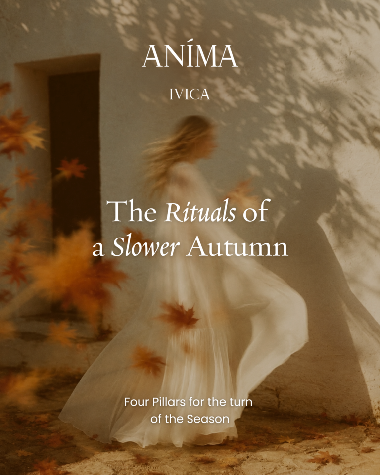 A woman in flowing white fabric walks past a sunlit stone wall scattered with autumn leaves
